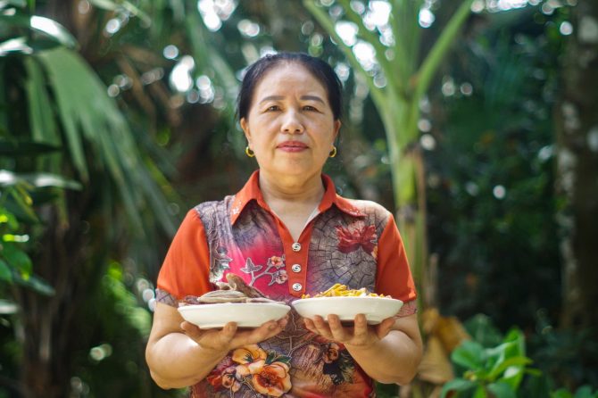 Mother of Phạm Hữu Tình, pilot farm manager, presenting two fruit products from the farm: dried banana (on the left) and jackfruit (on the right)